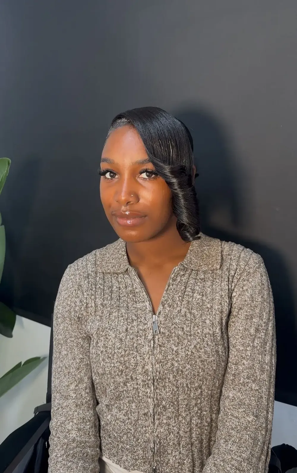 Client seated beside a plant wearing a sleek side swoop with curls